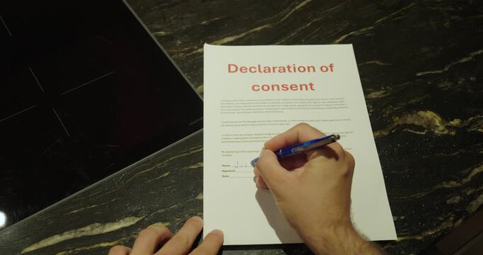 Close-up of a person signing a declaration of consent form with a blue pen. Concept of legal authorization, consent, agreements, compliance, and official paperwork.