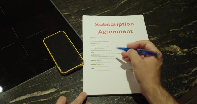 Close-up of a person reviewing and signing a mobile phone subscription agreement beside a smartphone. Concept of mobile contracts, service plans, telecommunications, and legal paperwork.