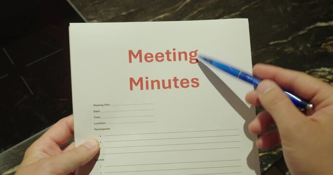 Close-up of a person writing on a meeting minutes template with a blue pen. Business concept of documentation, note taking, meeting records, and office organization.