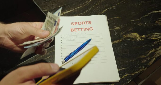 Close-up of a man using a smartphone for sports betting while holding cash beside a betting slip. Concept of online gambling, sports wagering, betting strategy, and mobile gaming.