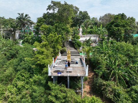 Aerial view of a viewpoint platform with two people standing on it, surrounded by lush tropical forest and greenery in Rawai, Phuket, Thailand.