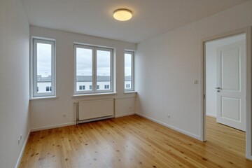 Fototapeta premium Empty room interior with white walls and wooden floor. Windows show suburban houses outside. Doorway opens to adjacent room. Modern apartment ready for furnishing or sale.