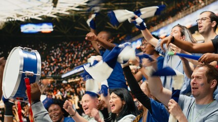 Diverse blue football supporters raising arms and chanting together in stadium stands during live soccer match with powerful crowd energy, passionate football fans gathered in excitement. © DC Studio