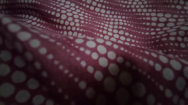 Close-up macro shot of a maroon fabric with white polka dots. The material displays fluid, natural ripples, creating an elegant contrast between light and shadow. Perfect for artistic backgrounds.