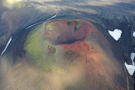 Aerial view of the vibrant red and green slopes of Raudaskal crater with patches of snow in Rangarthing ytra, Iceland.