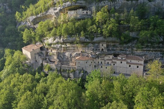Aerial view of the historic Hermitage of Santo Spirito a Maiella nestled into the rocky cliffs of the Majella mountains, surrounded by lush green forests in Roccamorice, Abruzzo, Italy.