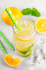 Fototapeta premium Close up of refreshing homemade lemonade with fresh lemon slices, mint leaves, ice cubes with soda water and paper straws served in glass with water droplets on gray kitchen counter background.