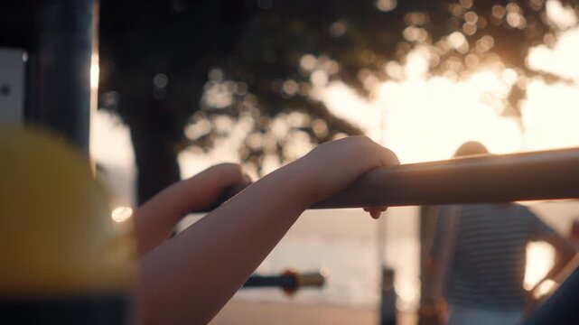 Child holds onto horizontal bar at sunset near water during evening playtime at the park