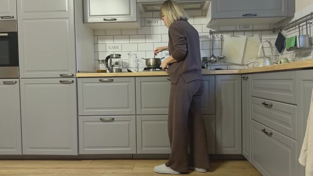 Woman gently stirring food in pot on stove. Peaceful kitchen routine and everyday cooking process