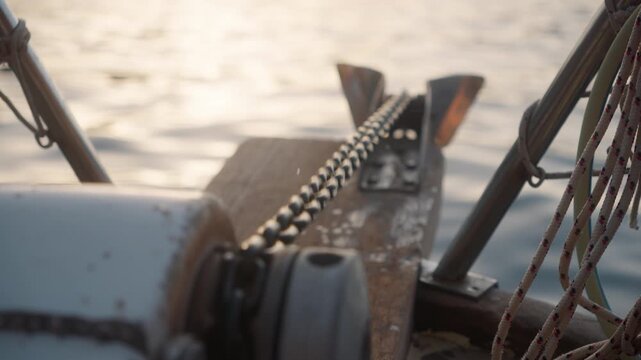 Close view of a boat anchor chain and winch on the water during sunset, showing the calm surface and soft light reflecting
