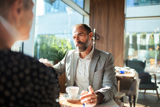 Mature businessman meeting client over coffee in modern cafe