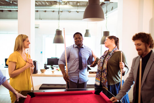Coworkers playing billiards in a modern office break room