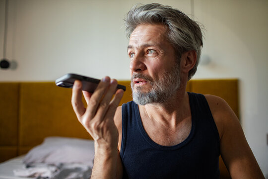 Middle-aged man recording voice message in bedroom at home