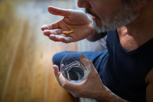 Middle-aged man taking pills with water at home