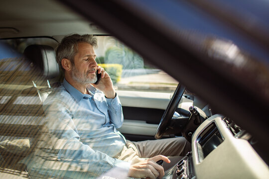 Mature businessman talking on smartphone in driver's seat of car
