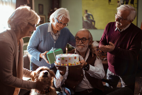Senior friends celebrating a birthday at home with cake and gifts