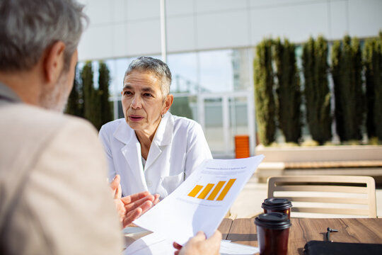 Senior doctor consulting patient outdoors with health report