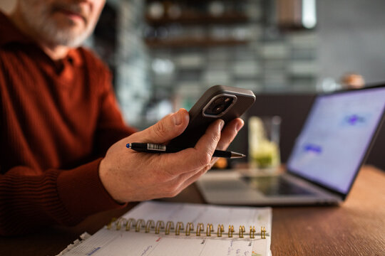 Mature man using smartphone while working at home office desk