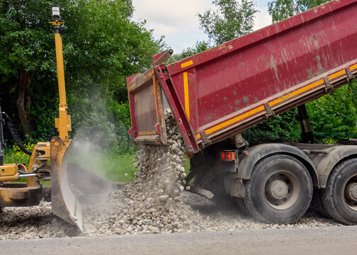 Dump truck unloading crushed stone or gravel next to a bulldozer blade at a road construction site