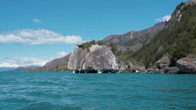 Wide shot of the iconic Marble Chapel rock formation with water-eroded textures, situated in the turquoise glacial waters of General Carrera Lake, Patagonia, Chile.