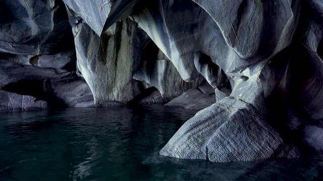 Close-up view inside a natural cave featuring intricate, water-eroded stone textures and deep shadows over dark water, highlighting the geological rock formations.