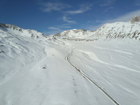 Aerial view of Campo Imperatore featuring a winding road cutting through the vast snow-covered plateau in L'Aquila, Abruzzo, Italy.