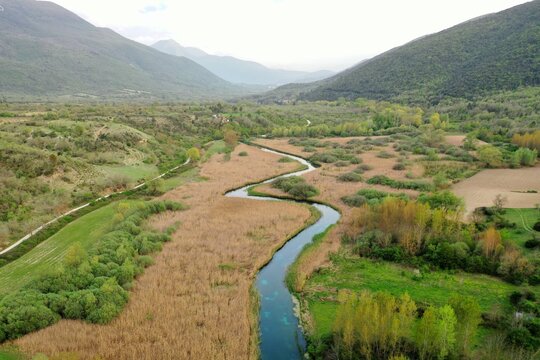 Aerial view of the Tirino River winding through the lush green valley and wetlands of Capestrano, Abruzzo, Italy.