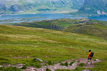 Obraz premium Hiker in Orange Jacket Overlooking Lofoten Islands Mountain Valley and Fjord