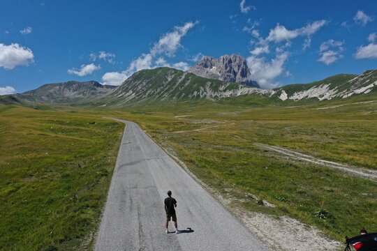 Aerial view of Campo Imperatore with a person standing on a road amidst the vast grassy plains and rugged mountains of L'Aquila, Abruzzo, Italy.