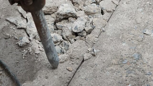 A jackhammer is being used to break up a concrete surface during a road repair construction