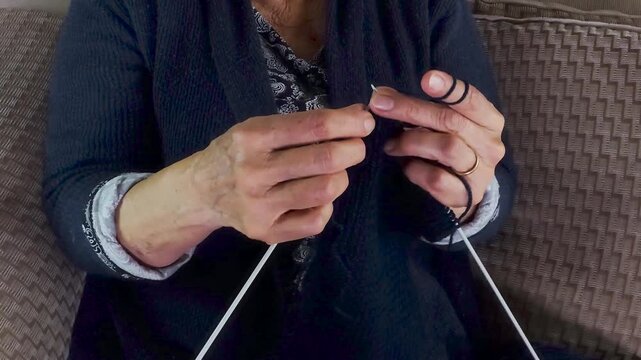 Elderly Hands Knitting Warm Clothing with Dark Wool Close-Up