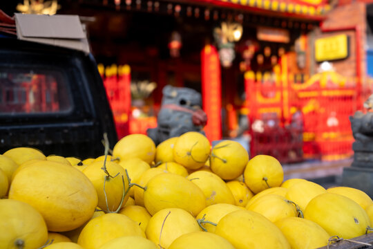 Fresh yellow canary melons displayed on a pickup truck bed at a traditional market with a red Chinese temple softly blurred in the background, Solo, Central Java, Indonesia.