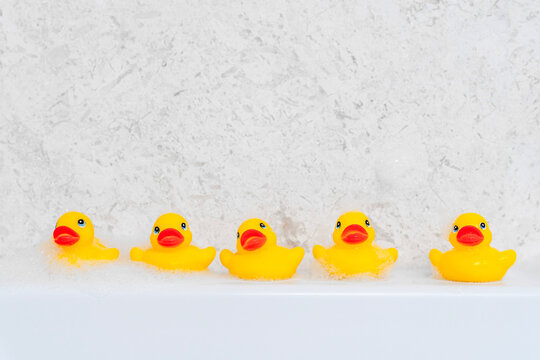 Row of five cheerful yellow rubber ducks lined up along the white edge of a bathtub in a playful bath scene.
