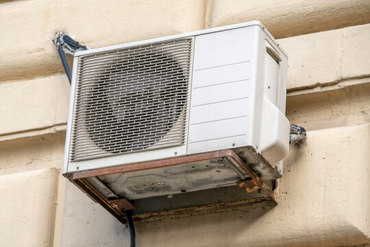 White outdoor air conditioning unit mounted on the beige wall of a building under bright daylight.