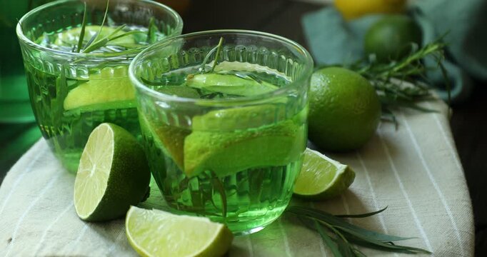 Tasty lemonade with tarragon in glasses, limes and fresh leaves on table, closeup