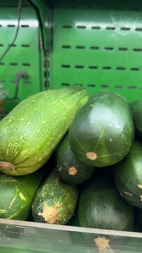 Zucchini squash lie in a tight stack on a metal supermarket shelf under bright indoor lighting, shot in vertical close-up for food or nutrition content.