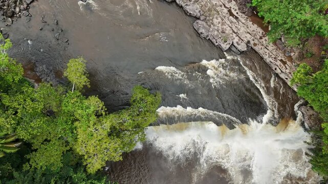 Aerial view of a waterfall surrounded by lush greenery and rocky terrain.
