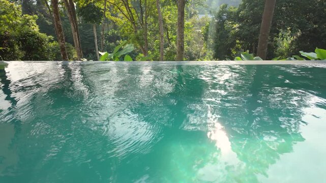 Tranquil infinity pool overlooking a lush tropical rainforest, with shimmering turquoise water reflecting the morning sunlight for a relaxing luxury nature retreat.