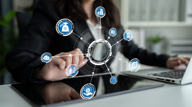 A businesswoman interacts with digital technology on a tablet, showcasing icons that illustrate concepts related to finance and investment. The scene emphasizes modern workspace innovations. Crux