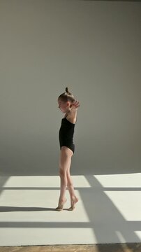 A little Caucasian girl gymnast in a black leotard does a backflip on a white background. 