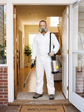 Pest control technician in protective suit standing in doorway of a house