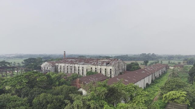 Ascending aerial view of Kushtia Sugar Mill showing the factory complex, production buildings, industrial infrastructure, and the surrounding landscape from an increasing altitude.