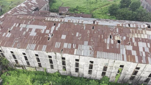 Half orbit aerial view of the abandoned Kushtia Sugar Mill, highlighting weathered factory buildings, broken roof sections, and the surrounding industrial site from multiple angles.