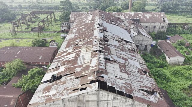Forward drone footage over the main Kushtia Sugar Mill building, revealing an aging corrugated metal roof, weathered industrial structures, and the surrounding factory complex.