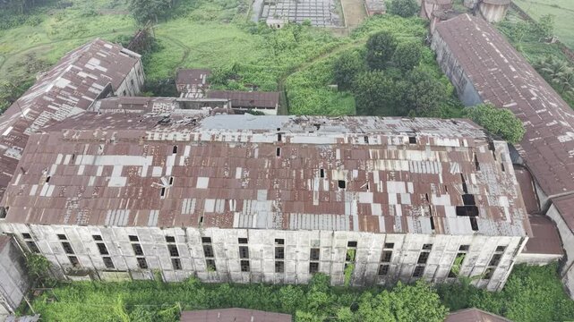 Backward aerial view of the abandoned Kushtia Sugar Mill, highlighting weathered factory roofs, broken roof sections, aging industrial buildings, and the inactive manufacturing site.