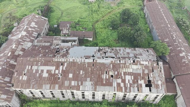 Direct overhead aerial view of the abandoned Kushtia Sugar Mill showing weathered factory roofs, broken roof sections, abandoned industrial buildings, and surrounding vegetation.