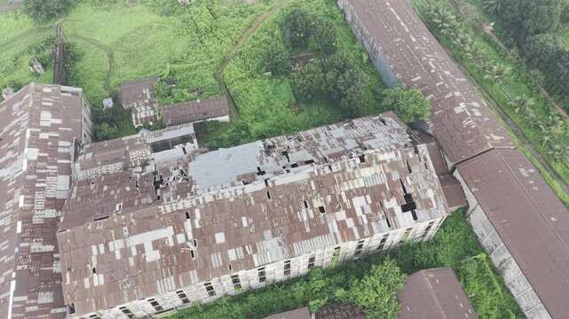 Top-down drone footage orbiting counterclockwise above the abandoned Kushtia Sugar Mill, revealing damaged factory roofs, deteriorated buildings, and the surrounding industrial property.