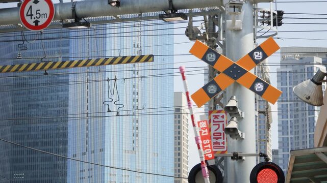 A close-up of railway crossing warning signs and barriers with yellow and orange caution markings on an urban Seoul street.