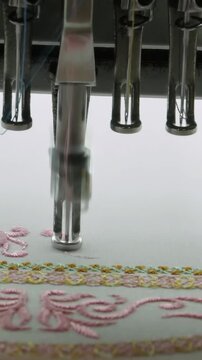 Industrial automatic computerized embroidery sewing machine deftly stitches intricate pink and gold patterns onto pristine white fabric.