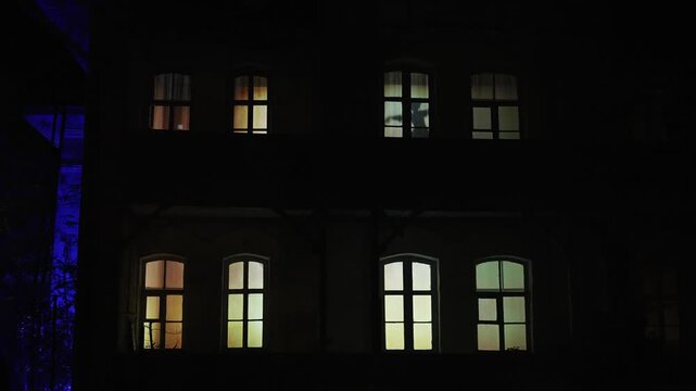 Silhouette of a ballerina in the window. A woman silhouette stands in a warmly lit window of a dark house at dusk